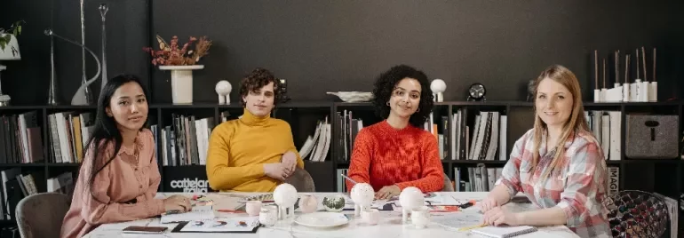 Four people sitting at a table in an office, surrounded by books and decor.